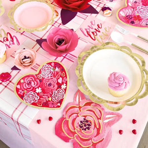 Decorative table setting with pink flowers, heart-shaped plates, and cupcakes on a pink and white checkered tablecloth.
