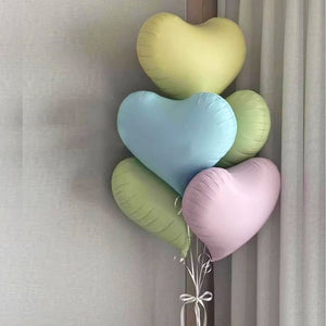 Heart-shaped balloons in pastel colors tied together against a neutral background
