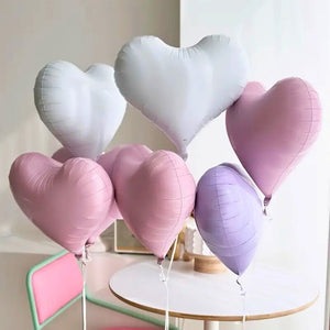 Heart-shaped balloons in white, pink, and purple on a table with a light background