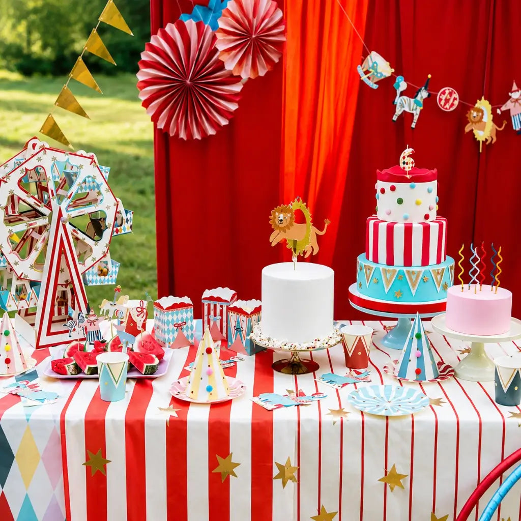 Carnival-themed party setup with cake, decorations, and tableware on a red and white striped tablecloth.