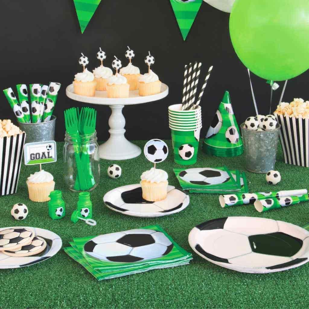 Table setting with soccer-themed party supplies including plates, cups, and napkins on a green surface.