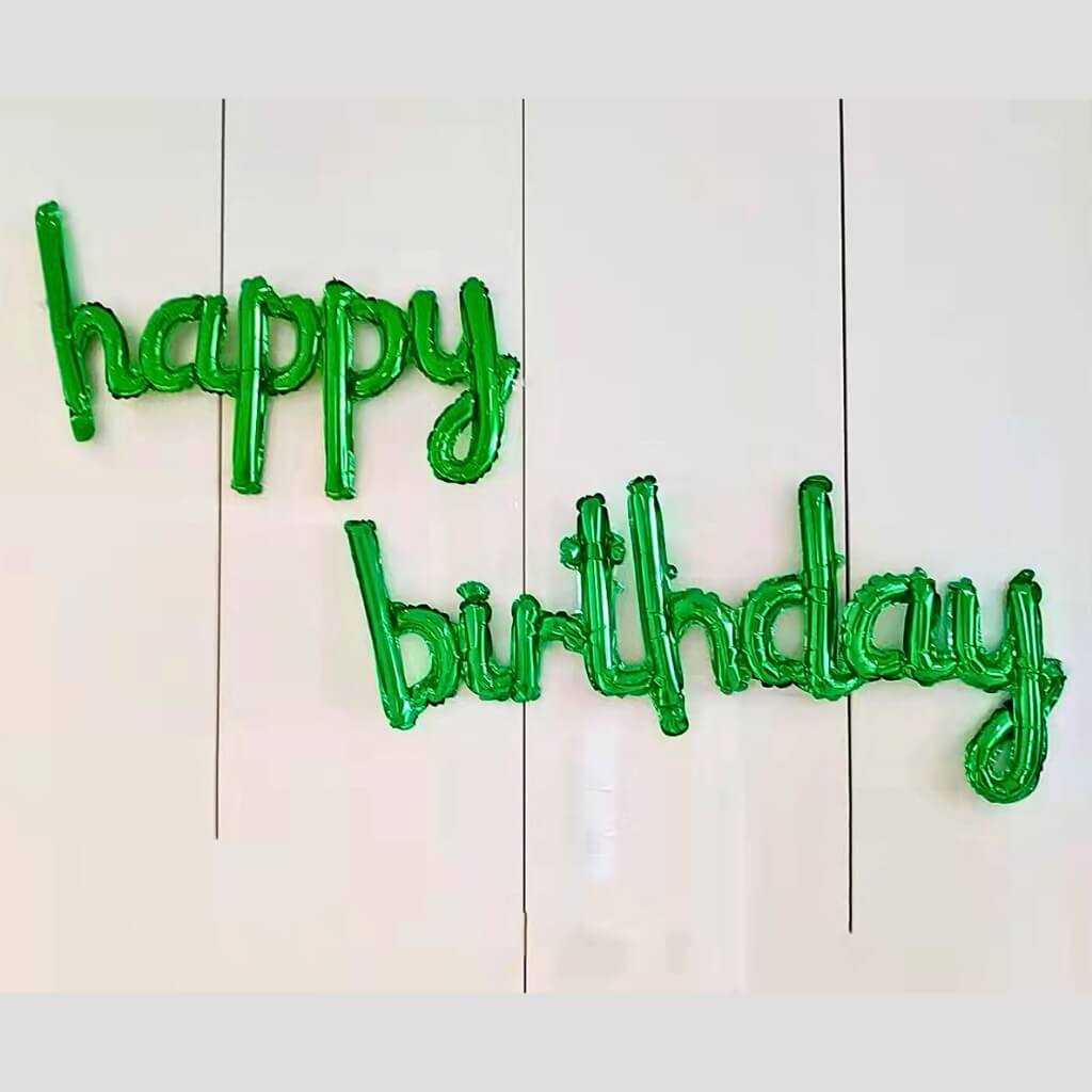 Green lowercase script happy birthday foil balloon banner hanging on wall