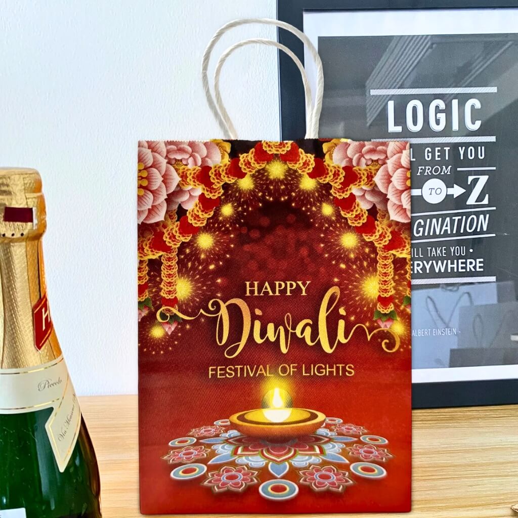 Red 'Happy Diwali' gift bag with a bottle of champagne on a wooden surface.