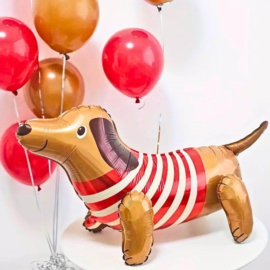 Inflatable dachshund balloon with a red and white striped sweater, surrounded by red and gold balloons on a white background.