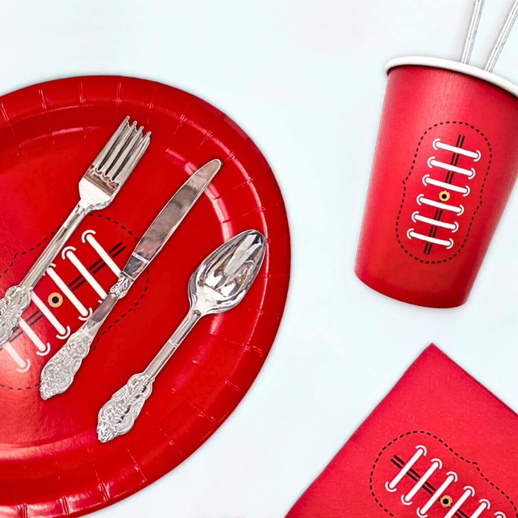 Red footy paper plate with silverware, red cup, and red napkin on a white background