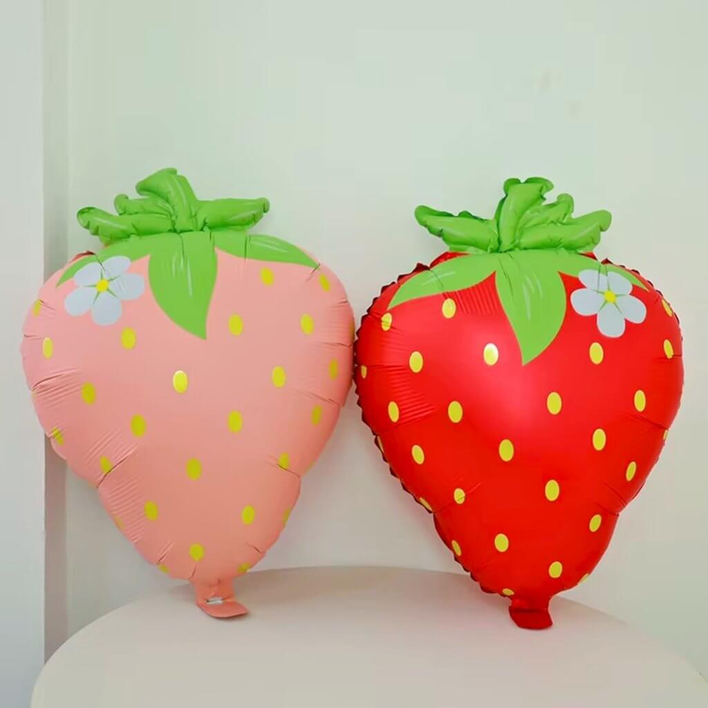 Two strawberry-shaped balloons, one pink and one red, on a white surface.