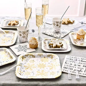 Table setting with snowflake-themed plates, cups, and napkins on a wooden table.